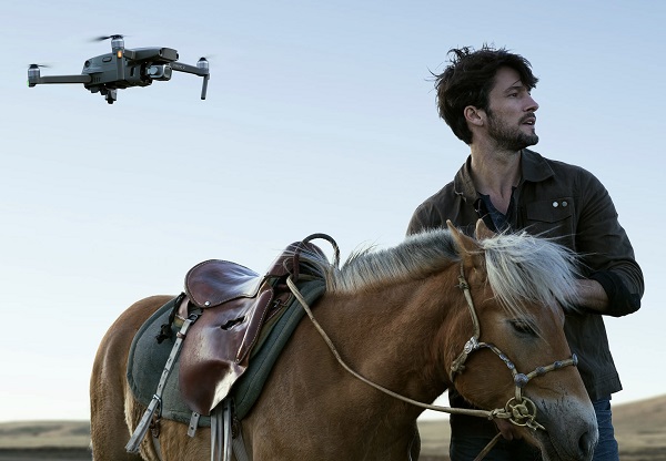 Portrait Of Young Handsome Jockey With His Race Horse & Drone Quadcopter With Digital Camera On His Top. 